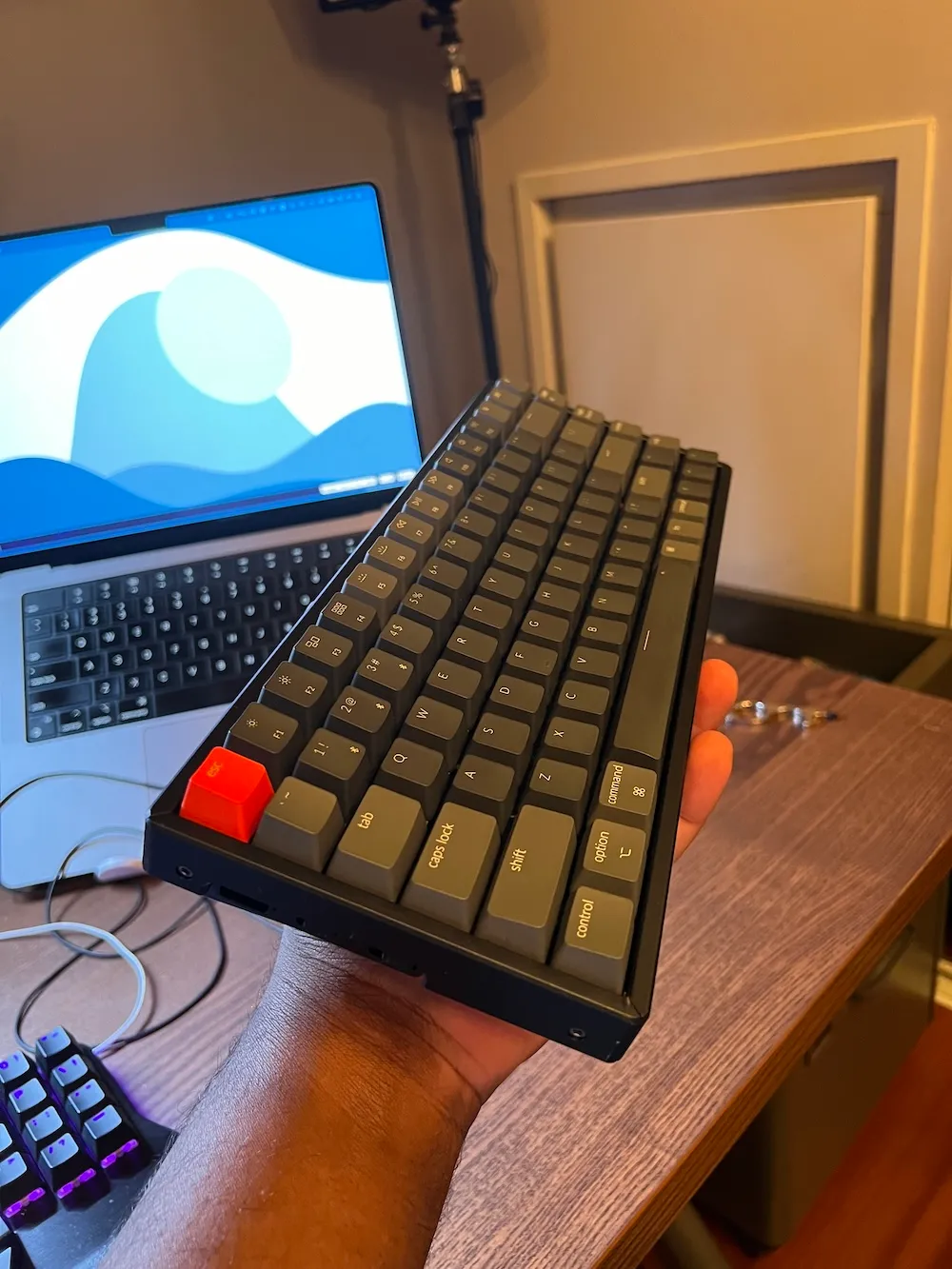 Photo du Keychron K2 de profil, dans ma main, face à mon MacBook Pro